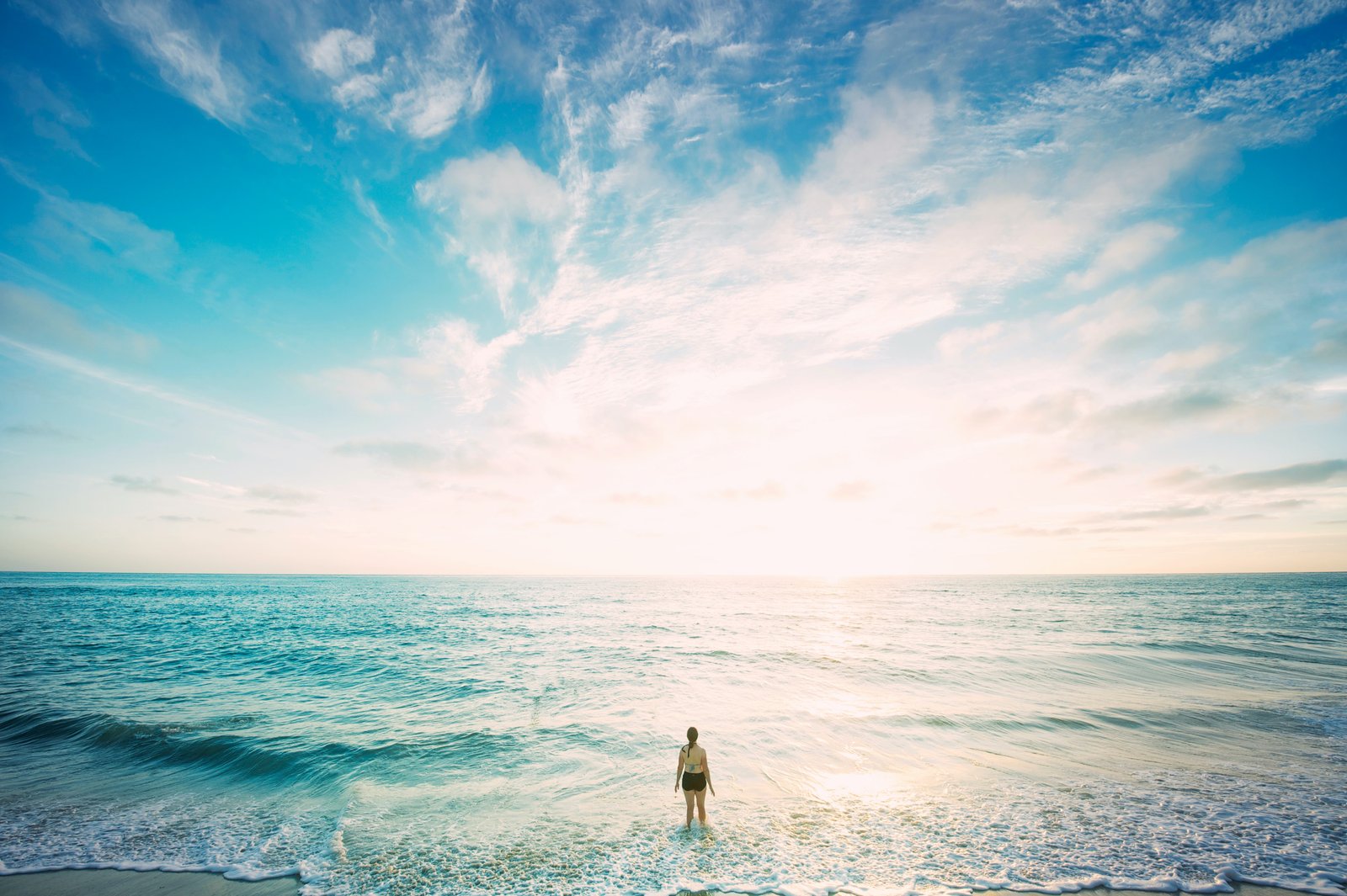 A lone figure standing in calm turquoise sea at dawn